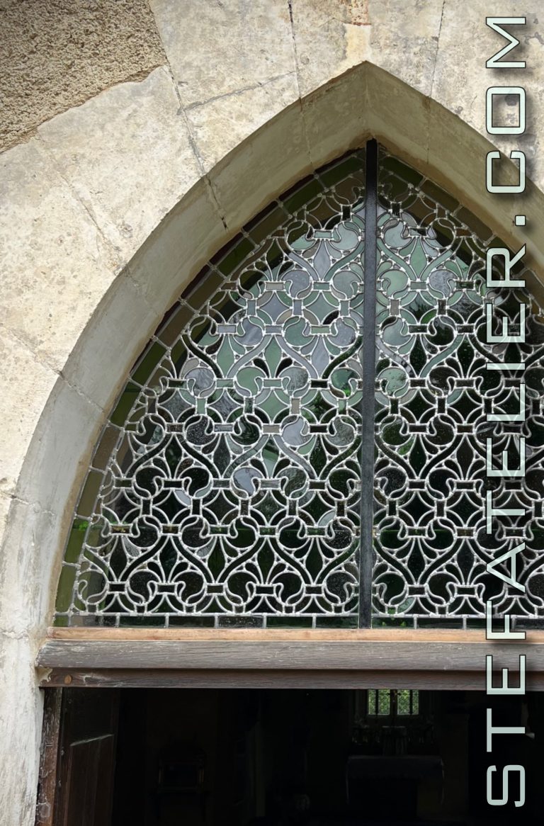 Plan rapproché des vitraux de l'imposte de porte de la chapelle notre dame de Bermont. Vitraux aux motifs de fleurs de lys entrelacés de cœurs. Ces motifs sont de style cistercien